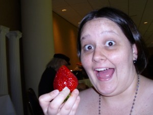 Alex holding a very large strawberry with a giant smile on her face.